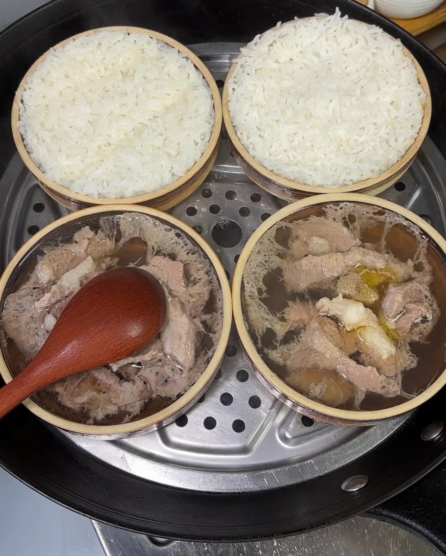 Dos pequeños cuencos de cerdo y arroz al vapor decorados con cebolletas frescas picadas.