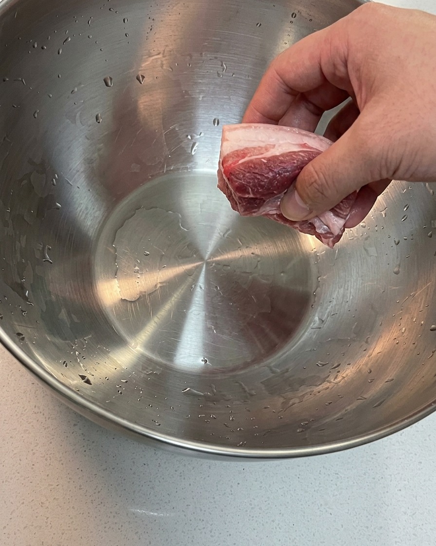 Panceta y hueso de espaldilla de cerdo en remojo en un cuenco con agua fría.