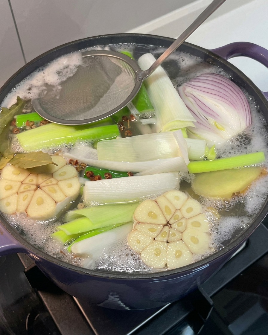 Espumadera retirando la espuma gris de la superficie del caldo.