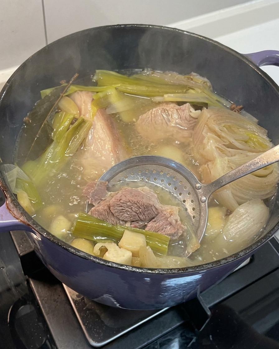 Retirando trozos de cebolla, ajo y jengibre cocidos del caldo terminado.