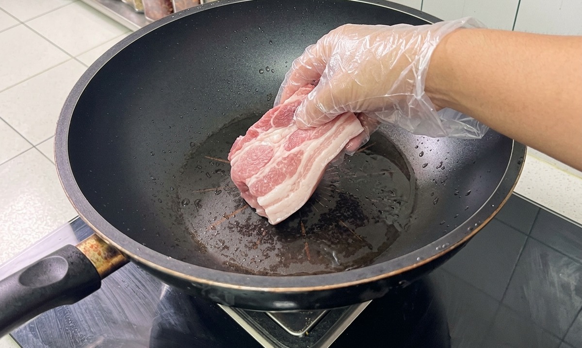Huesos y panceta de cerdo en un wok con agua y aromáticos siendo blanqueados.