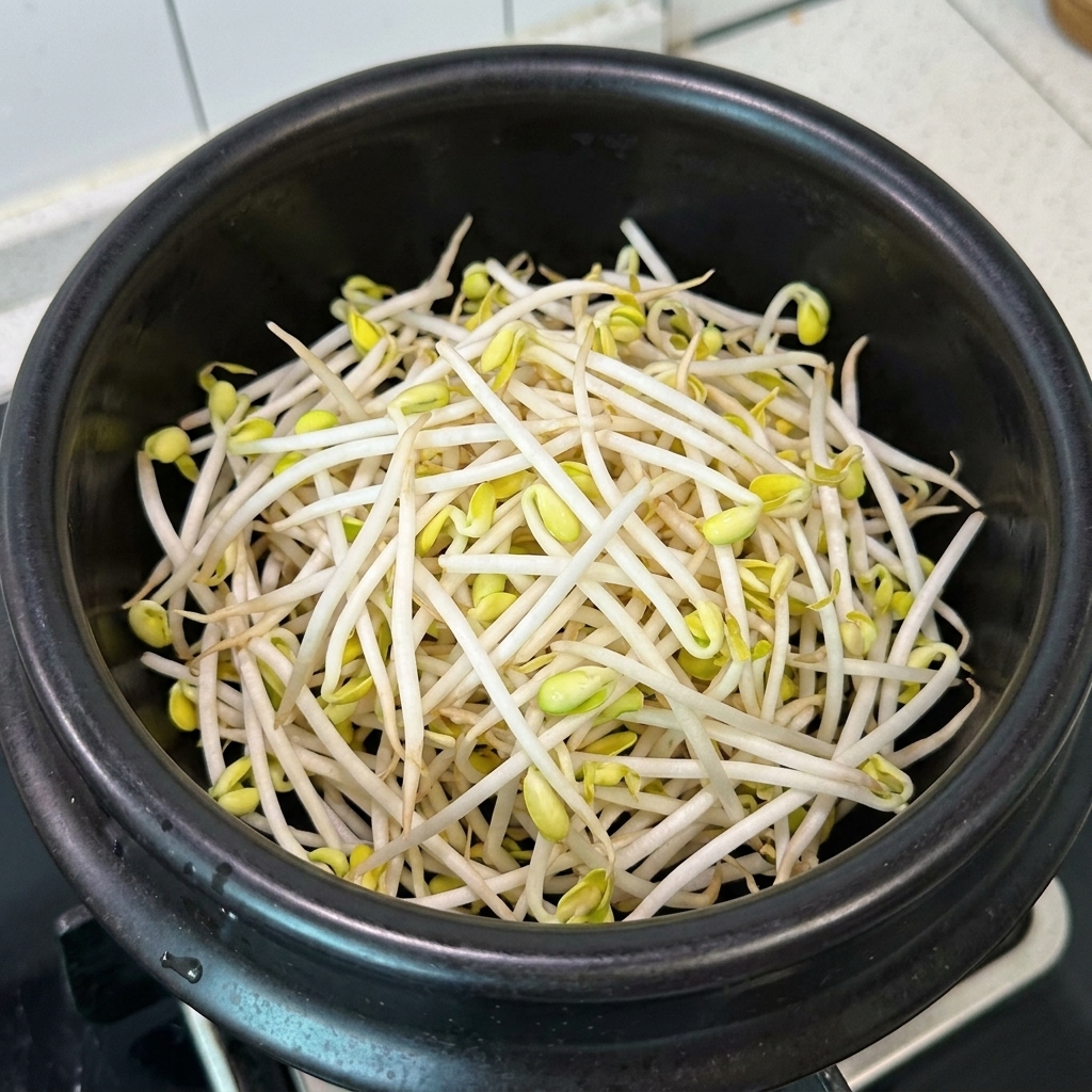 Brotes de soja y carne de cerdo desmenuzada dispuestos en una olla de barro negra.