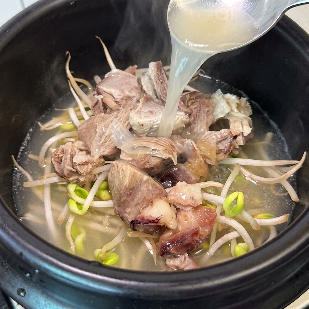 Un cucharón vertiendo caldo de huesos caliente en una olla de barro con carne y brotes de soja.