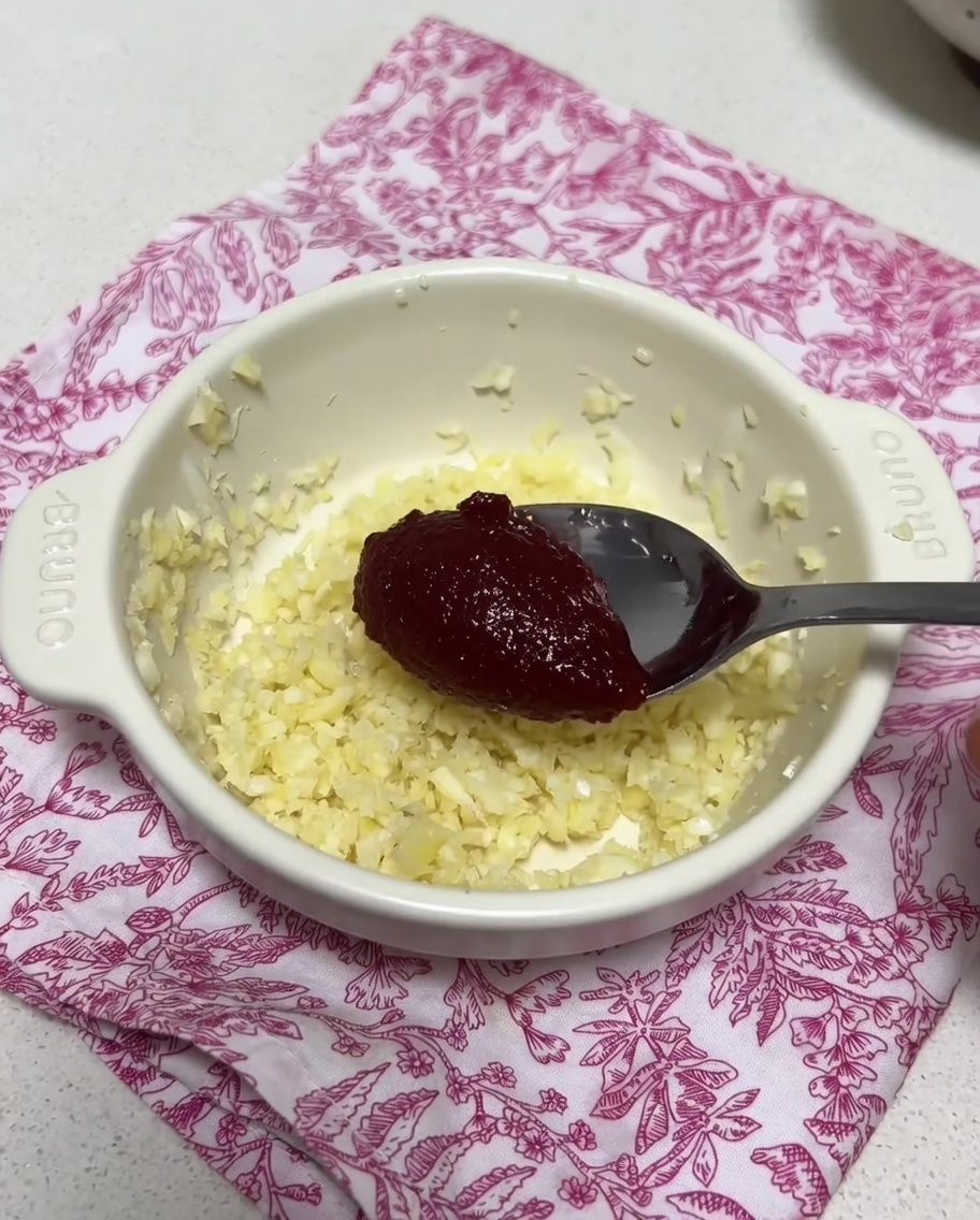 Un pequeño cuenco con ajo picado y una cucharada de pasta de chile coreana siendo mezclados con un poco de caldo.