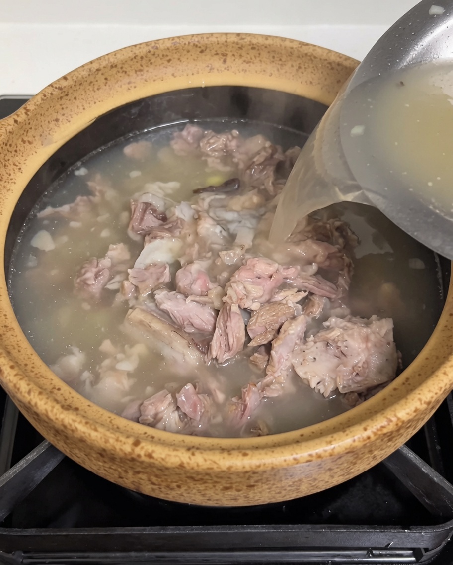 Caldo de carne caliente vertiéndose desde un recipiente de acero inoxidable a la cazuela con el cerdo y los brotes.