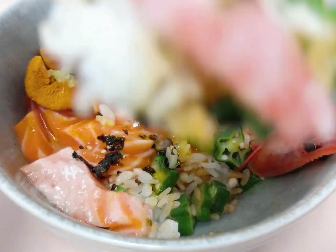 Ingredientes siendo colocados cuidadosamente sobre el arroz para crear la base del donburi.