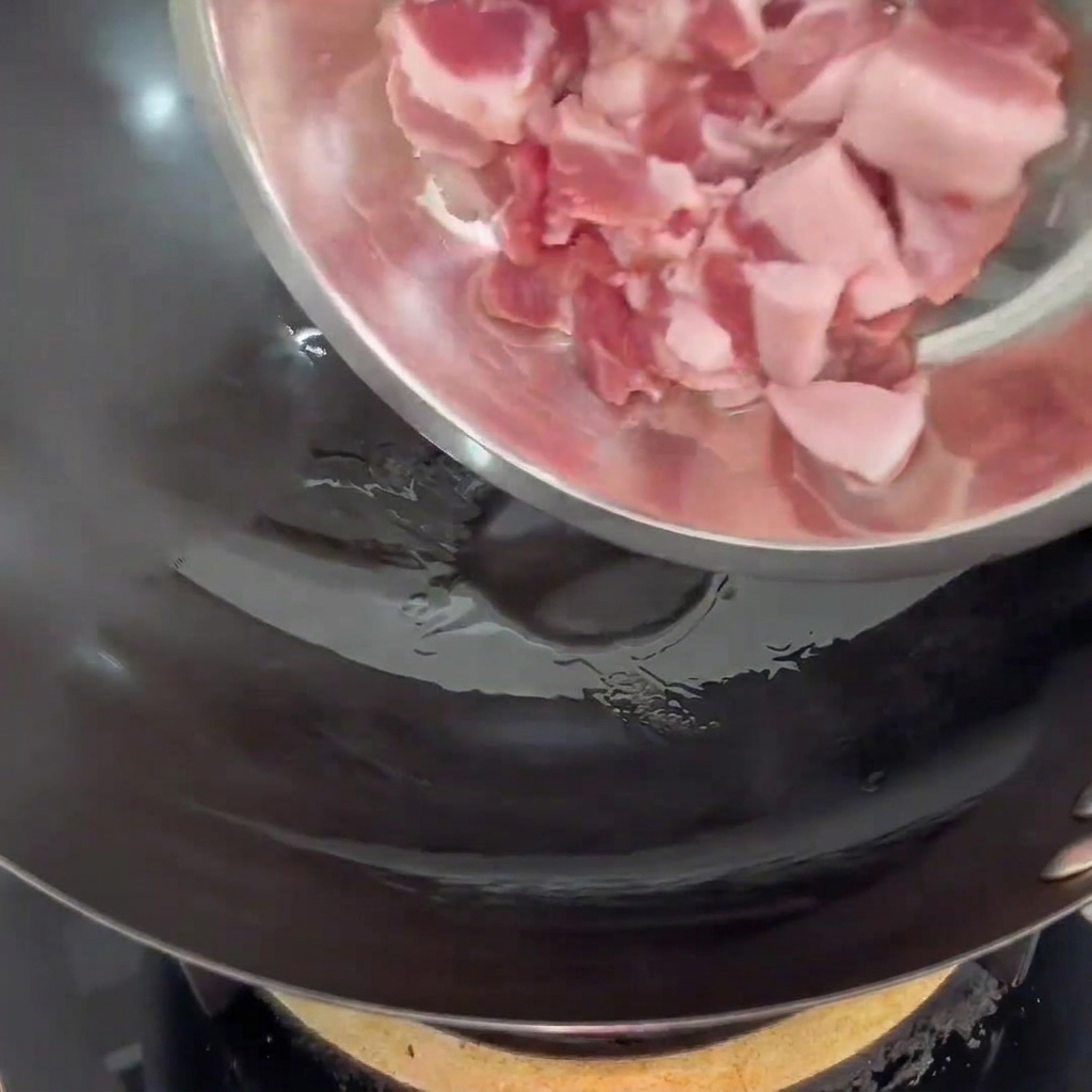 Rebanadas de panceta añadidas a un wok caliente con una fina capa de aceite.