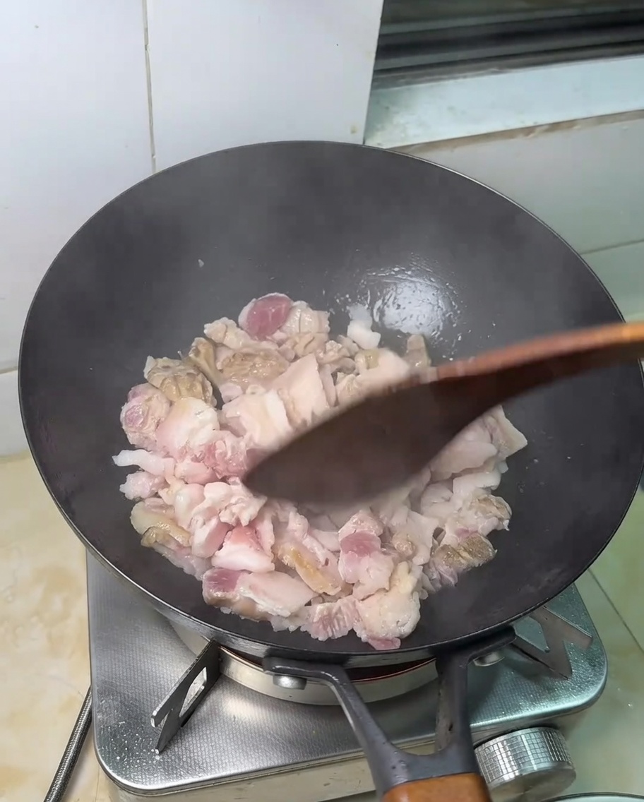 Láminas de panceta cruda friéndose en una sartén caliente.