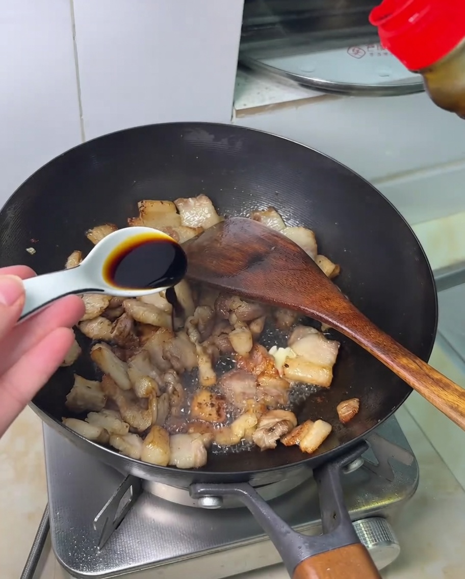 Salsa de soja siendo vertida sobre la panceta en un wok.