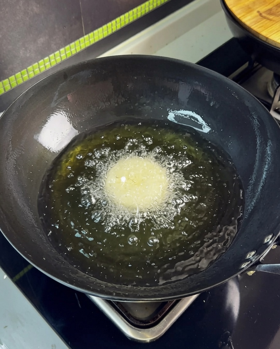 Una lámina de panceta siendo introducida en aceite caliente en un wok, creando burbujas vigorosas.