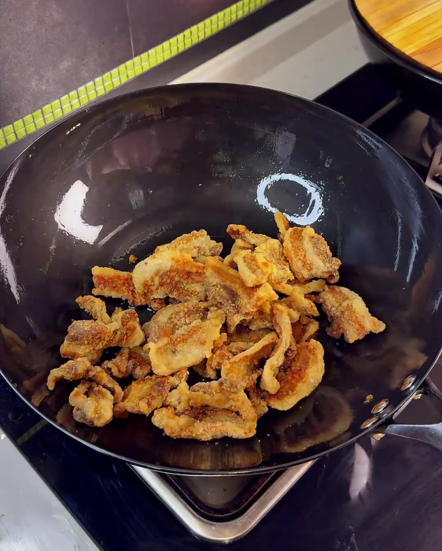 Panceta frita en un wok siendo salteada con ajo y la salsa de soja.