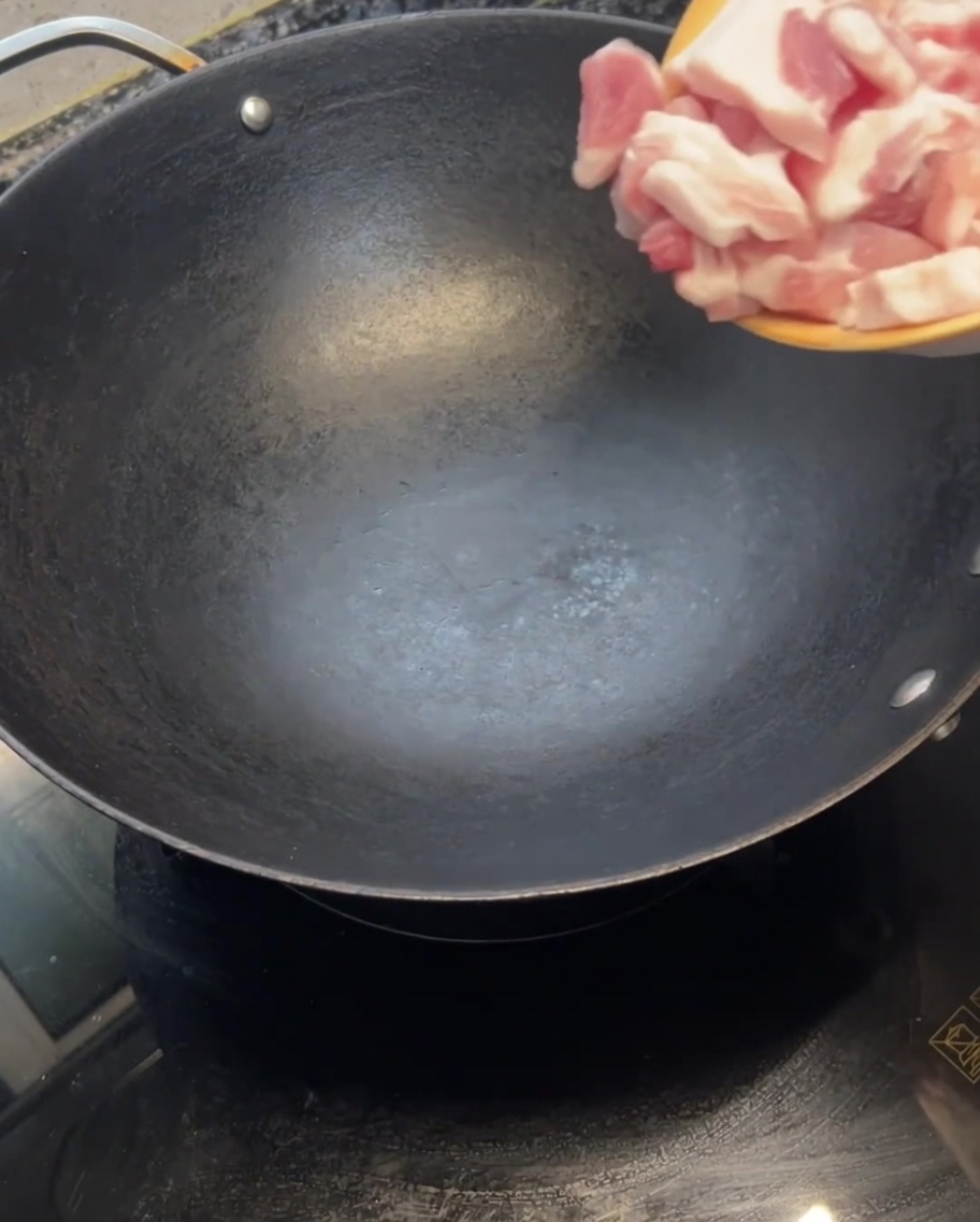 Láminas de panceta cruda siendo colocadas en un wok caliente y vacío.