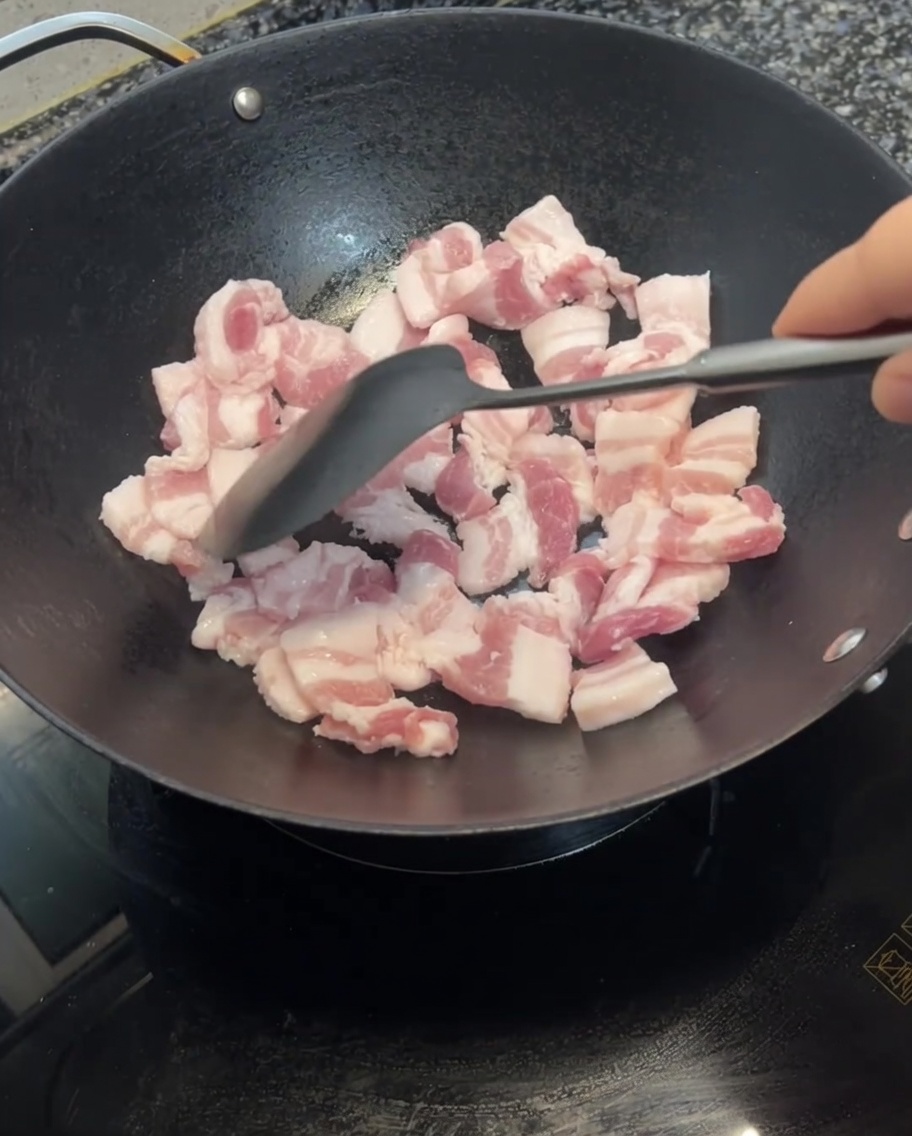 Láminas de panceta siendo salteadas en un wok con una espátula, mostrando signos de dorado.