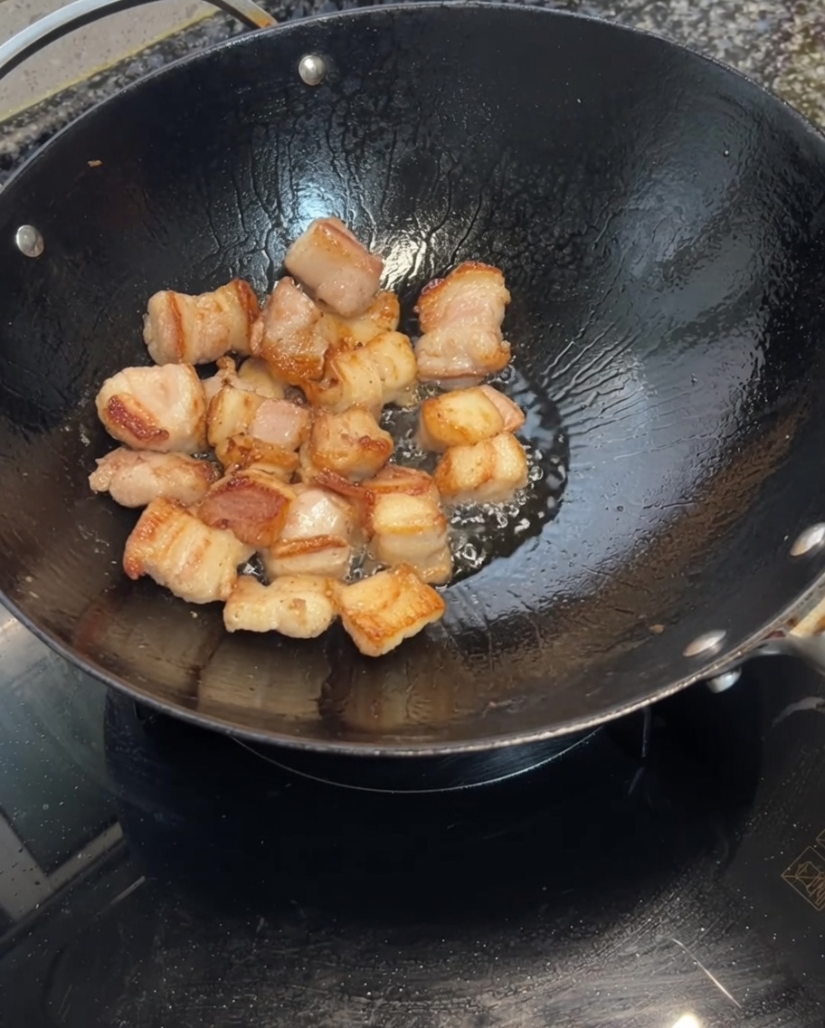 Dientes de ajo siendo añadidos al wok con la panceta dorada.