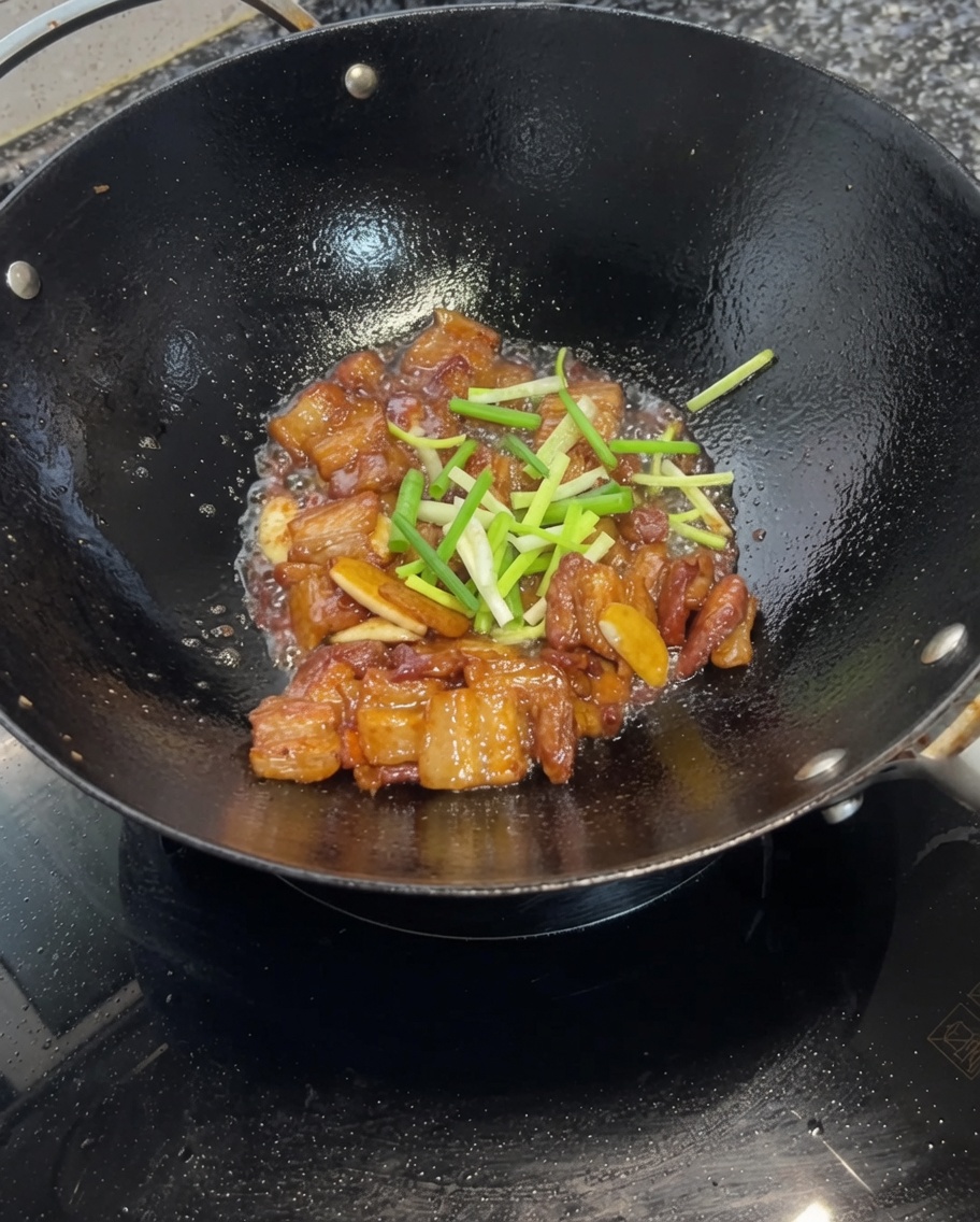 Segmentos de cebollino picado siendo mezclados con la panceta glaseada en el wok.