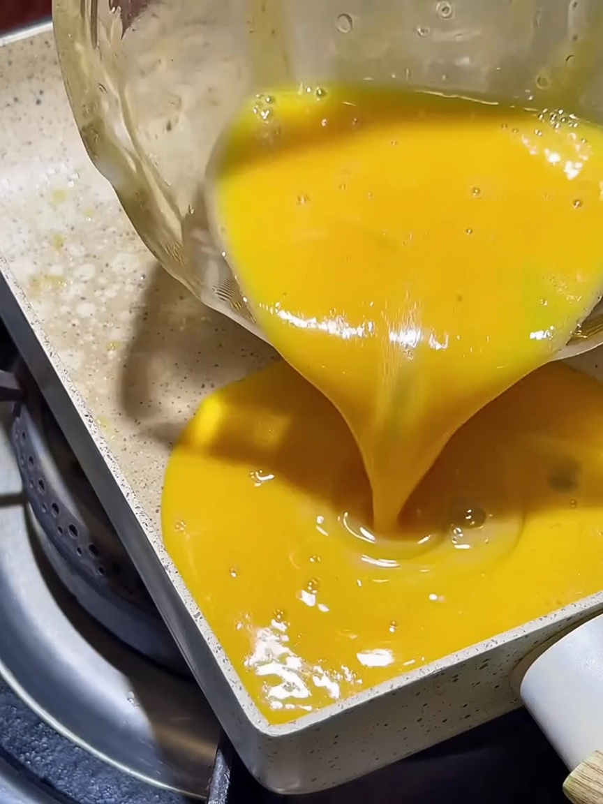 Mezcla de huevo batido extendiéndose uniformemente en una sartén cuadrada antiadherente.