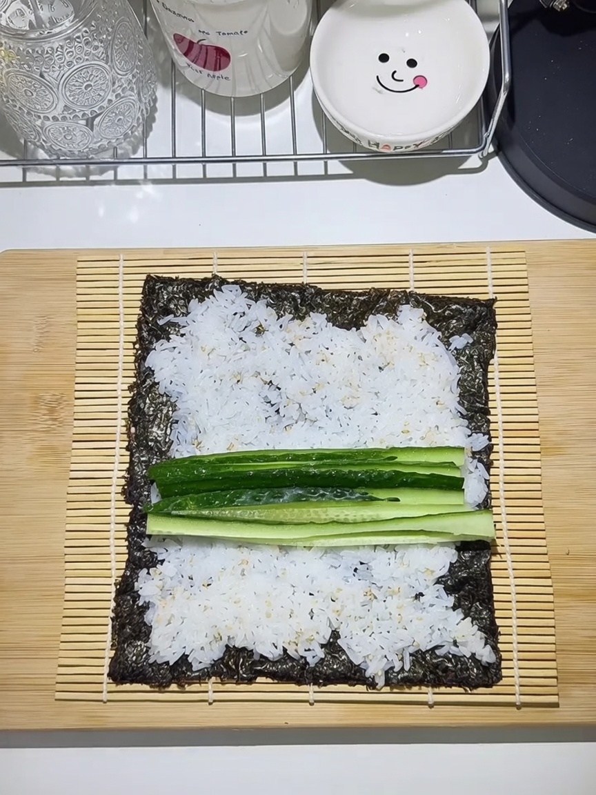 Una esterilla de bambú con una hoja de alga, cubierta con arroz y capas de pepino, zanahoria, huevo y tiras de ternera.