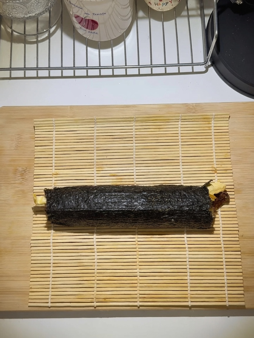 Un gimbap enrollado firmemente sobre una esterilla de bambú.