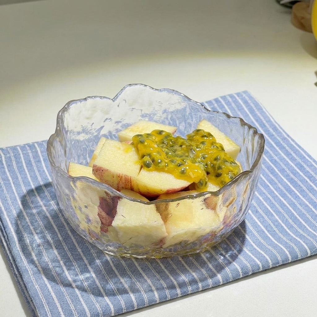 Un cuenco de cristal lleno de manzanas rojas troceadas cubiertas con pulpa amarilla de maracuyá y rociadas con miel.