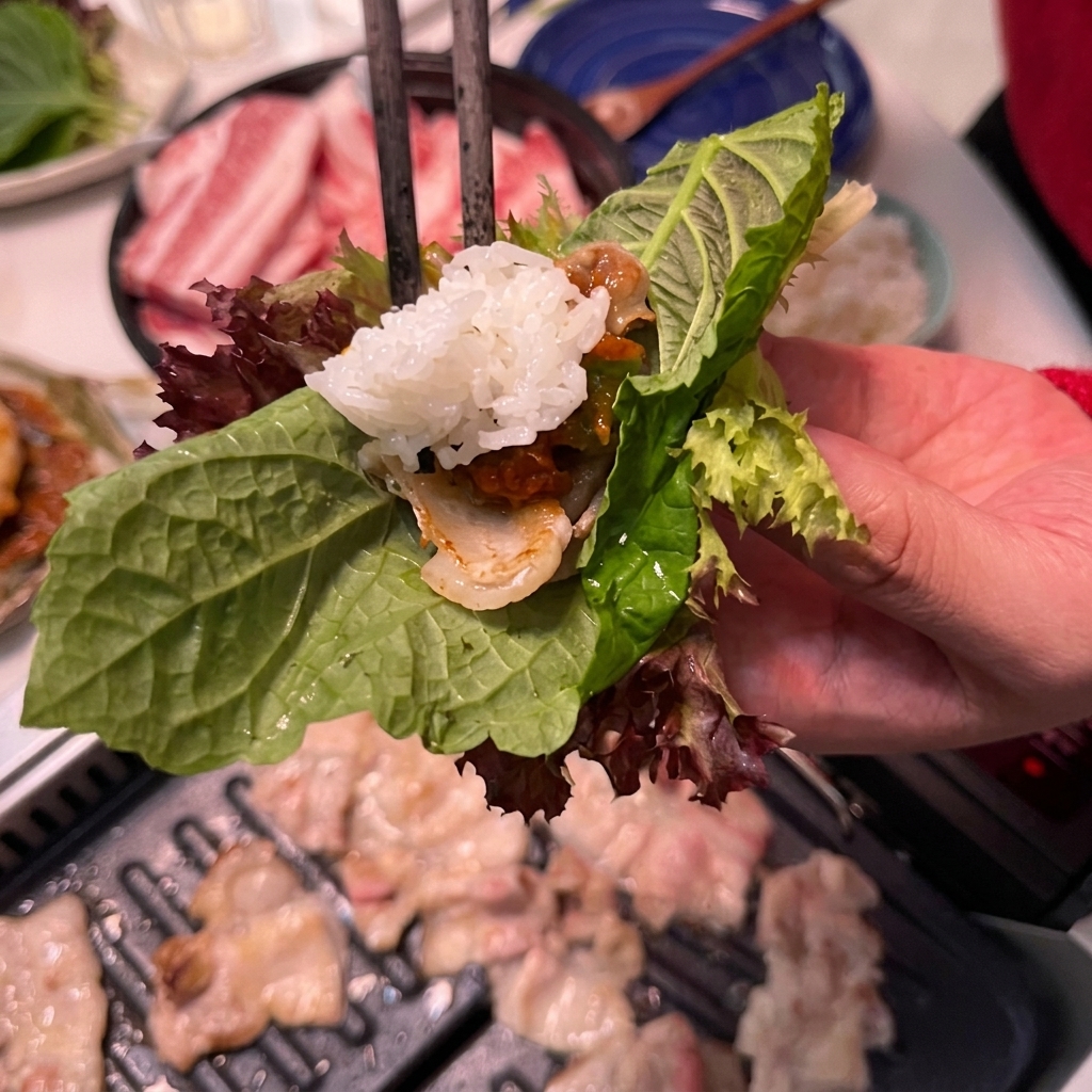 Una cucharada de arroz blanco siendo añadida a un wrap de lechuga con cerdo y salsa.