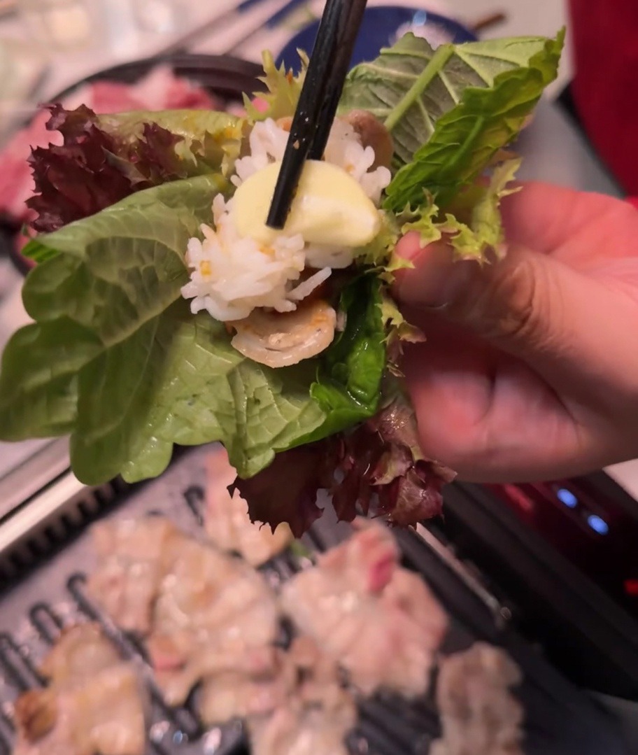 Una mano sosteniendo un wrap de lechuga y perilla con carne, arroz, pasta picante y ajo.