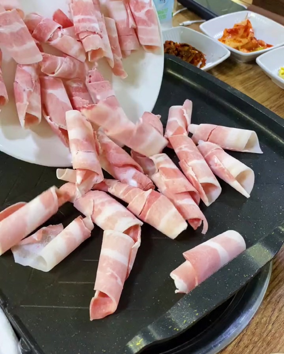 Rebanadas de panceta cruda colocadas sobre una plancha caliente.