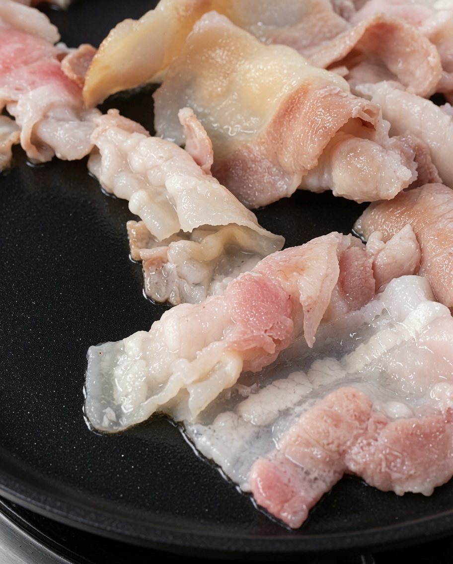 Rebanadas de panceta asada doradas sobre la plancha.