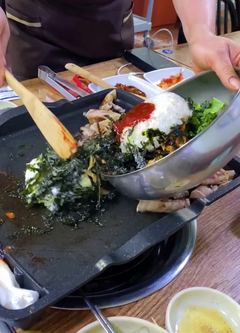Arroz, vegetales y algas vertidos desde un bol metálico a la plancha con la carne.