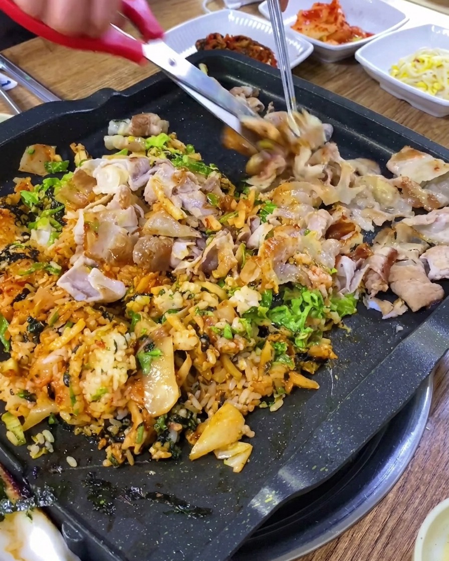 Tijeras de cocina cortando la panceta asada en trozos pequeños sobre la plancha.