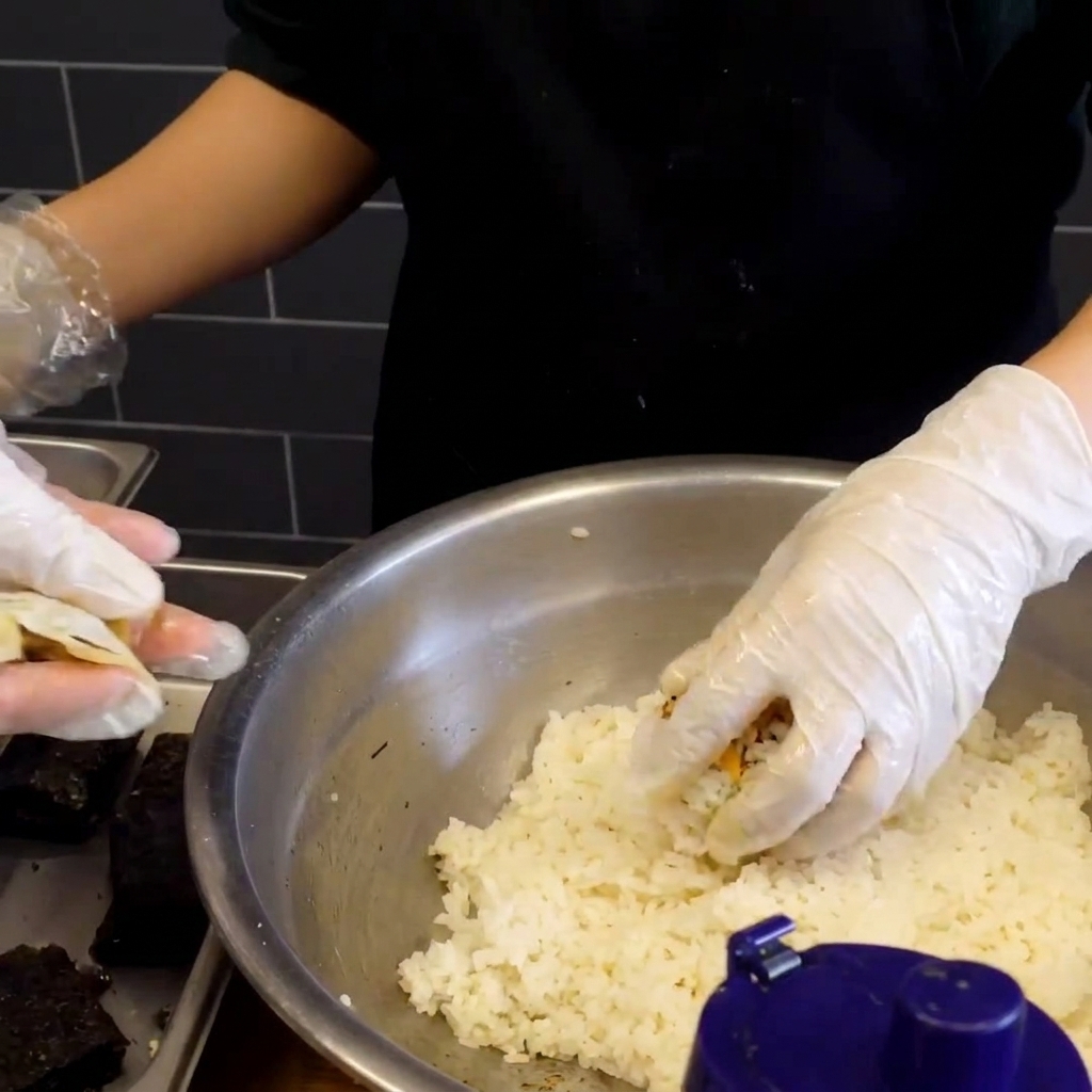 Una bola de arroz pegajoso recién formada con un pequeño cuadrado de alga seca oscura presionada sobre su superficie.