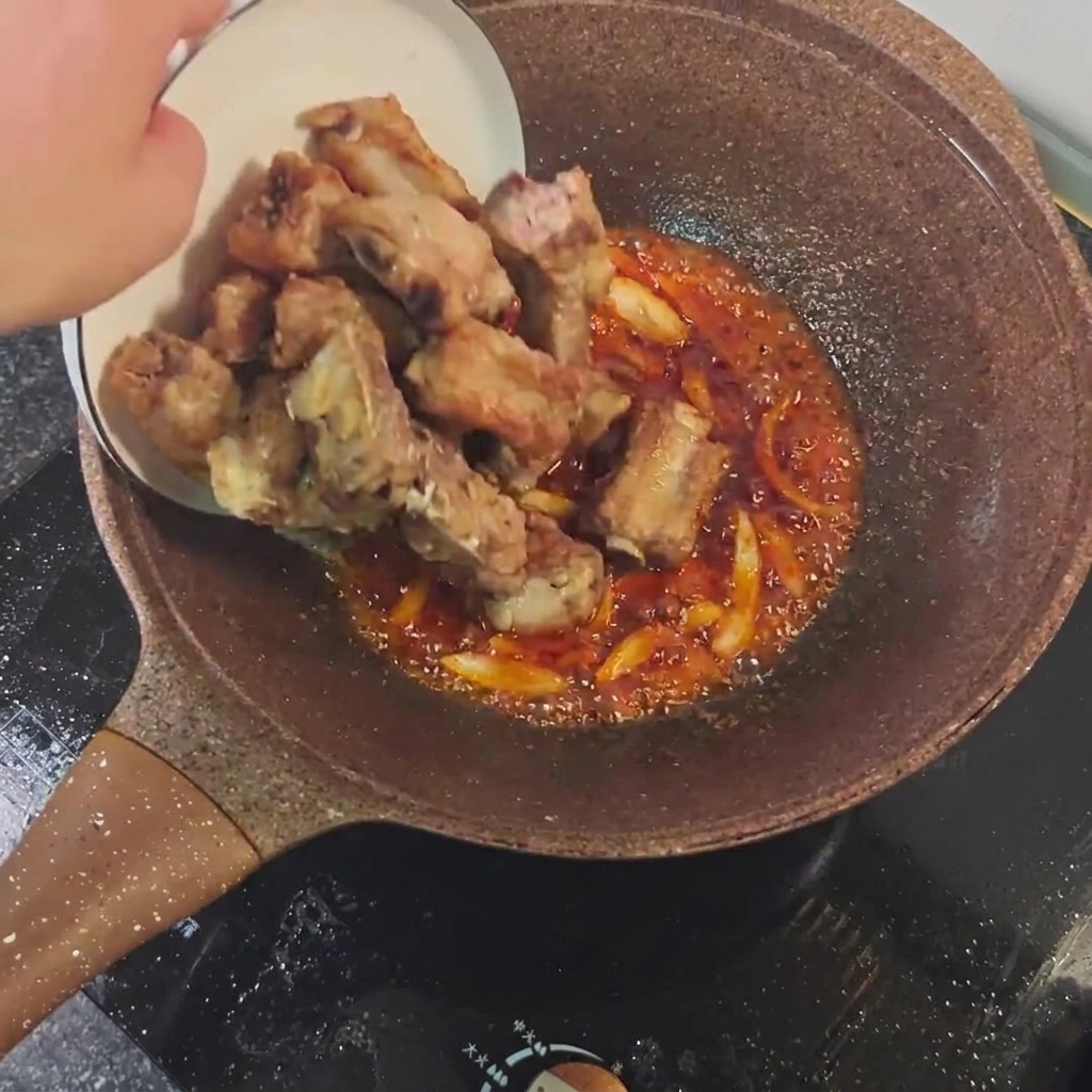 Costillas fritas mezclándose con la salsa picante en la sartén.