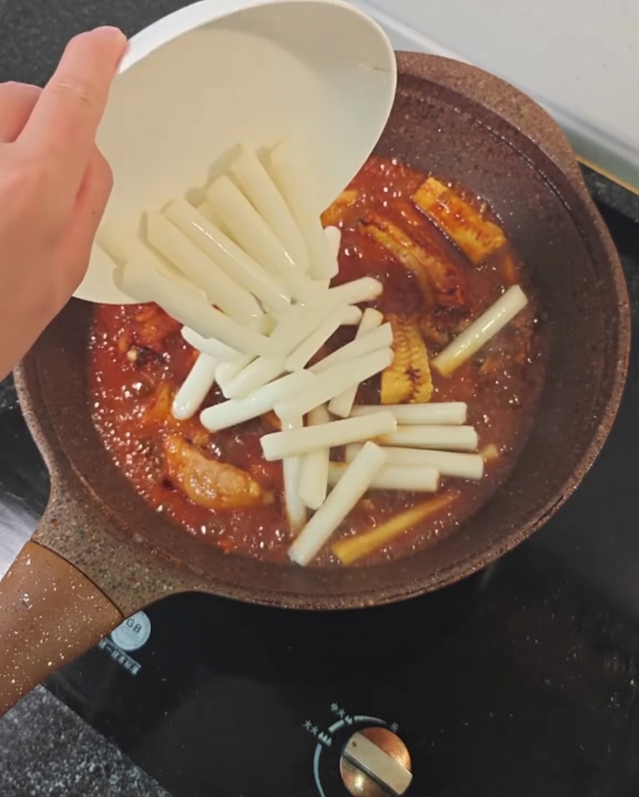 Pasteles de arroz siendo añadidos a la sartén con las costillas.
