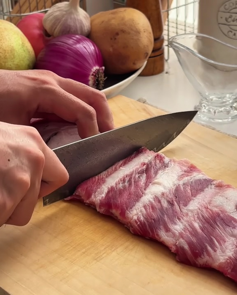 Primer plano de un chef cortando un costillar de cerdo en una tabla de madera.