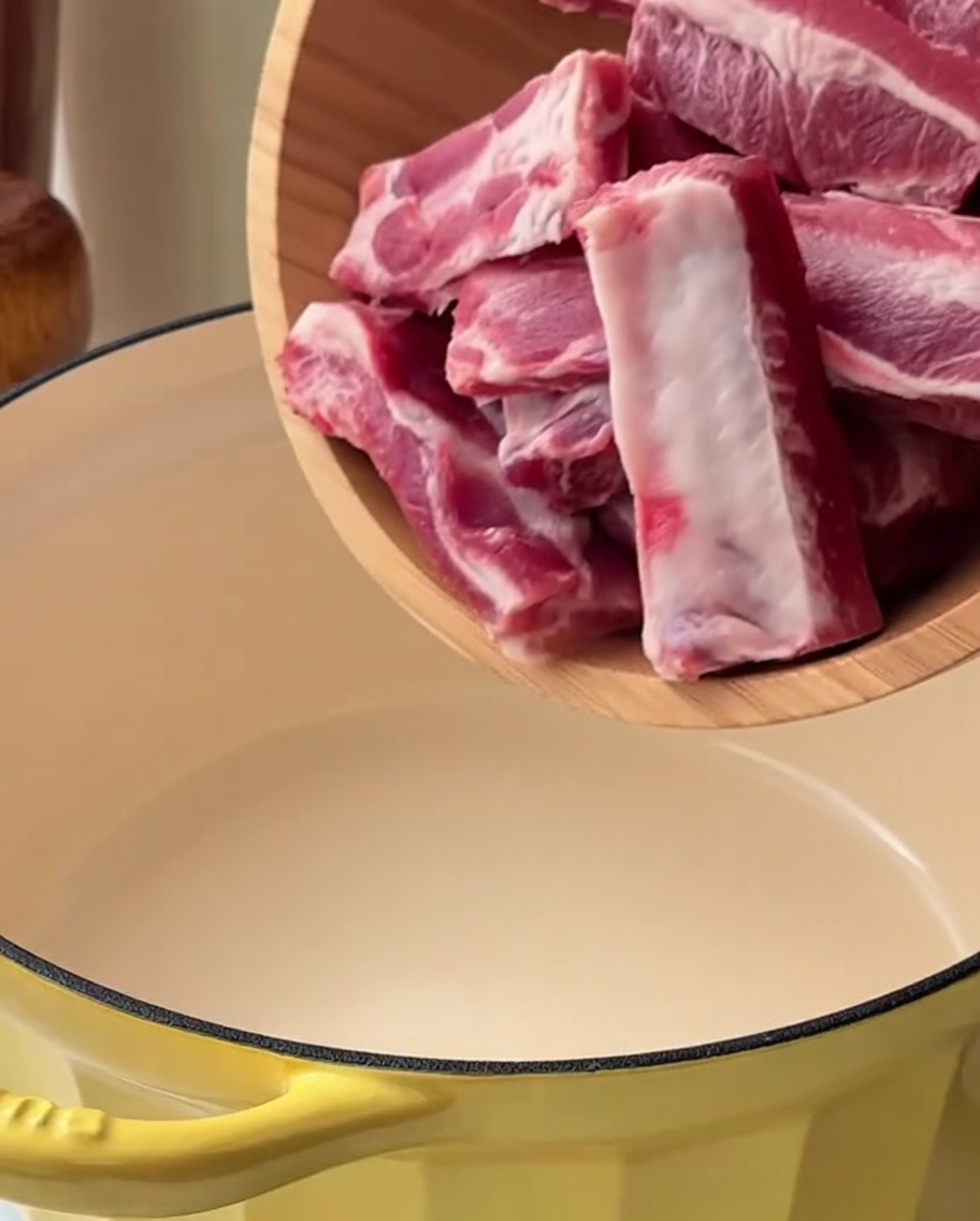 Trozos de costillas de cerdo en una olla amarilla sumergidos en agua con cebolleta y jengibre.