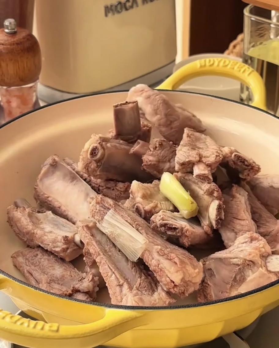 Marinado picante vertiéndose sobre costillas de cerdo blanqueadas en una olla.