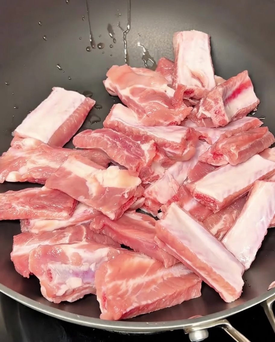 Costillas de cerdo hirviendo en agua con aromáticos durante el proceso de blanqueado.