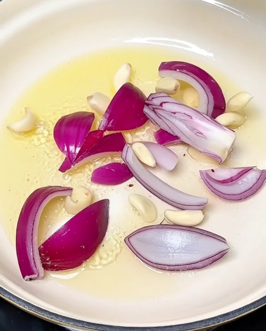 Cebolla en rodajas y ajos siendo salteados en una olla caliente.