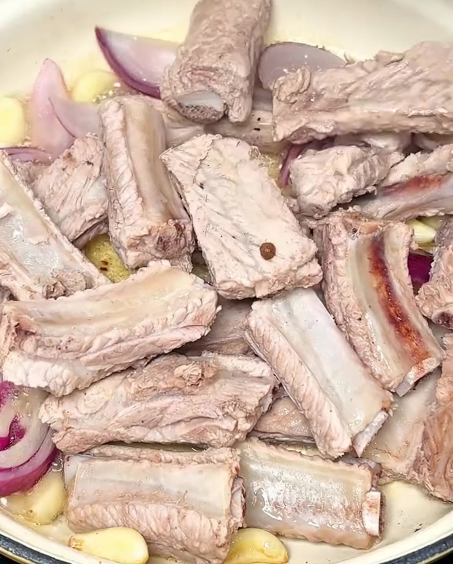 Costillas de cerdo blanqueadas siendo integradas en la olla con los aromáticos.