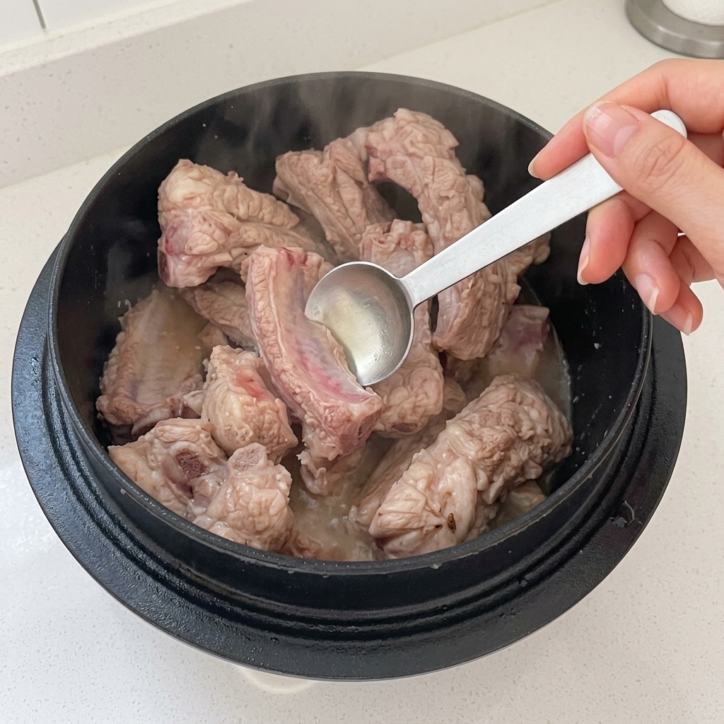 Vinagre siendo añadido a una olla con costillas de cerdo sofritas.