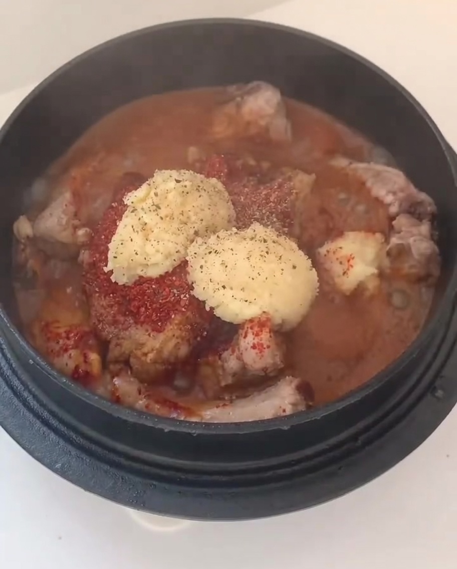 Cebolla blanca picada y rodajas de cebollino añadidas sobre las costillas sazonadas en una olla.