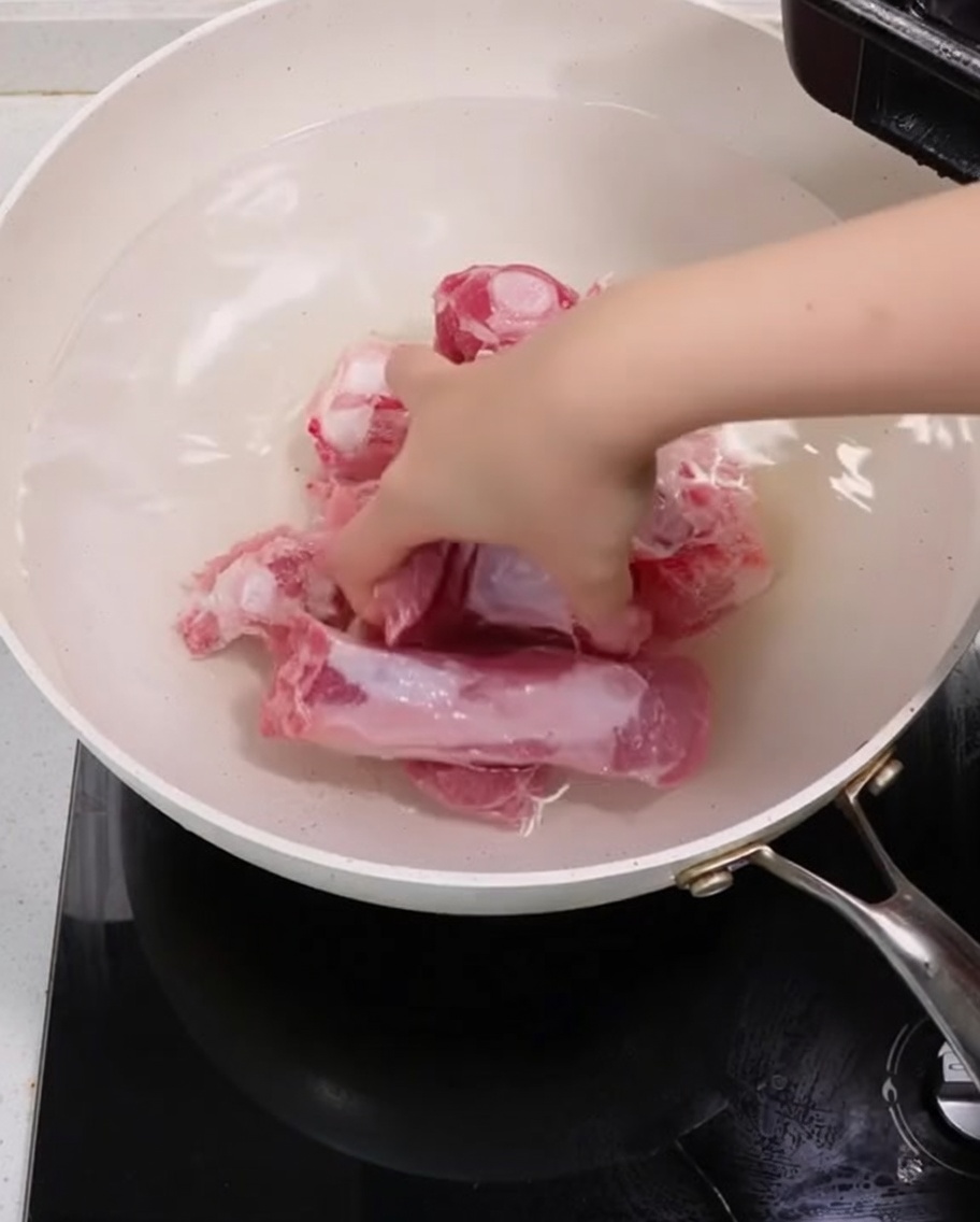 Costillas de cerdo hirviendo en una olla con rodajas de cebolleta y jengibre para blanquear.