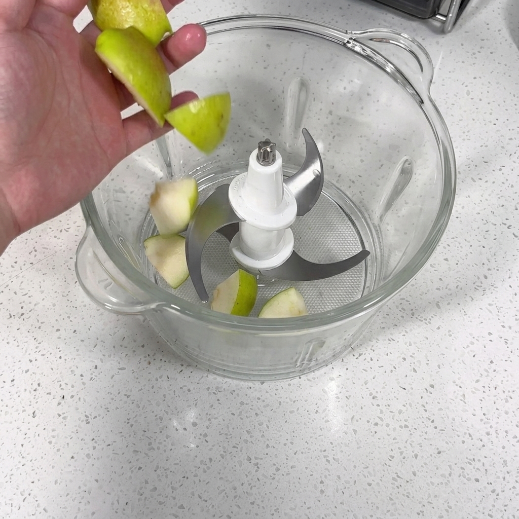 Procesador de alimentos lleno con trozos de manzana, pera, ajo y cebolla siendo triturados hasta obtener un puré.
