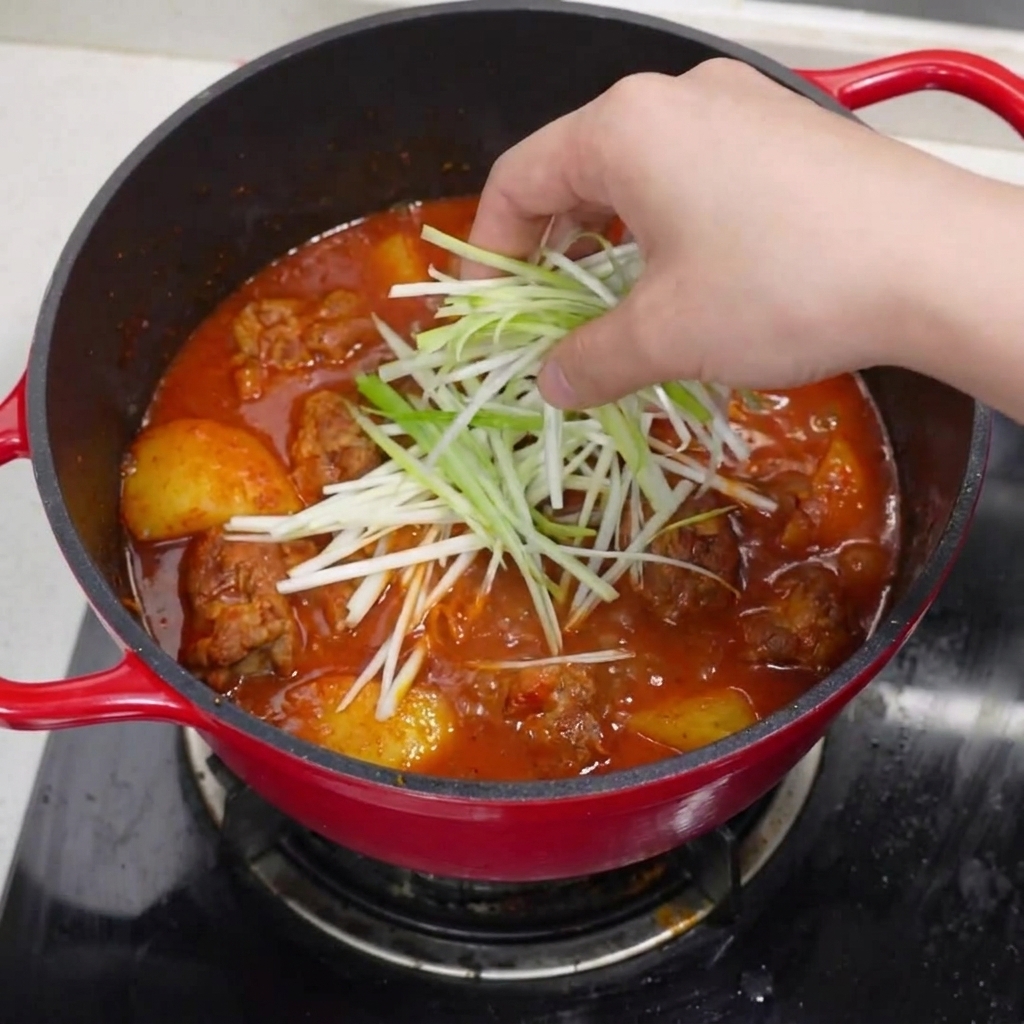 La olla terminada con costillas de cerdo, decorada con cebolleta picada, rodajas de chile rojo y pimienta negra.