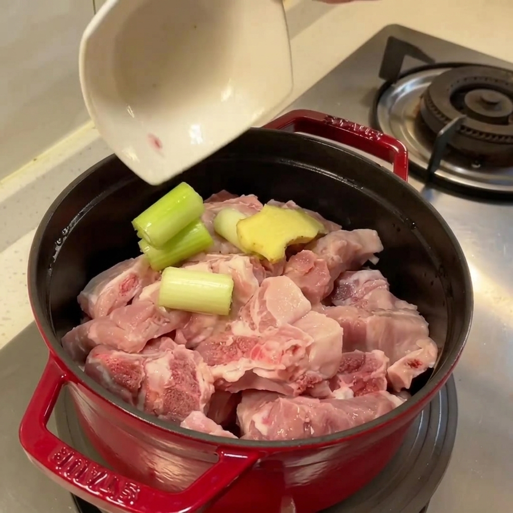 Olla llena de costillas de cerdo crudas, jengibre y cebolla verde listas para hervir.