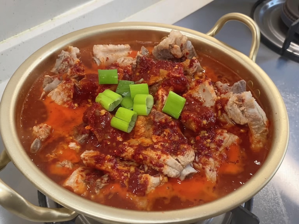 Olla de costillas en proceso de guisado siendo espolvoreada con cebollas verdes frescas picadas.