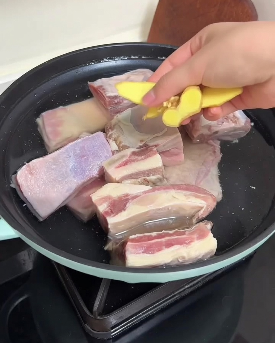 Costillas en una olla con agua y jengibre preparándose para el blanqueado.