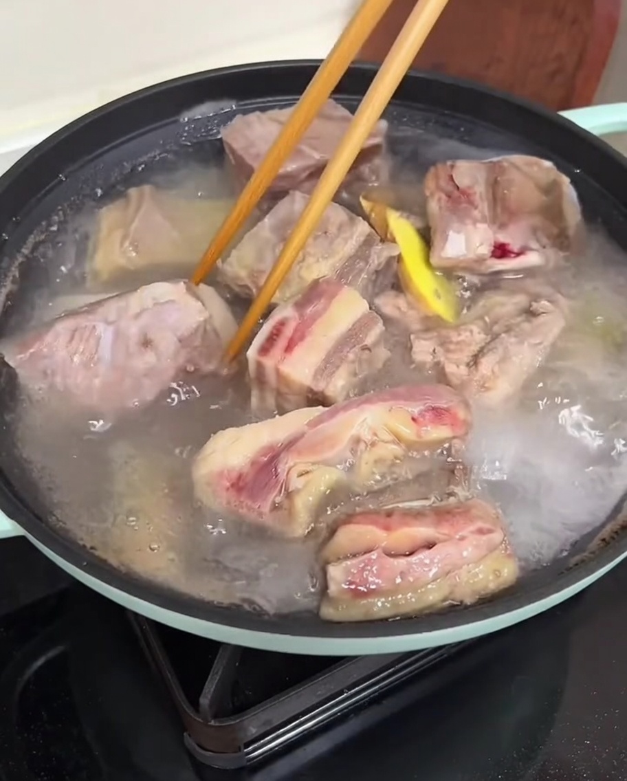 Manos usando palillos para limpiar costillas blanqueadas bajo agua corriente.