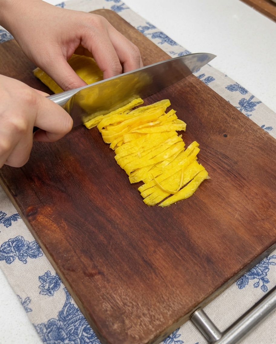 Primer plano cortando una crepa de huevo cocida en tiras uniformes.