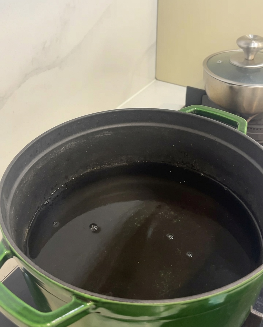 Trozos de costillas cortas de res crudas dentro de una olla grande verde llena de agua fría.