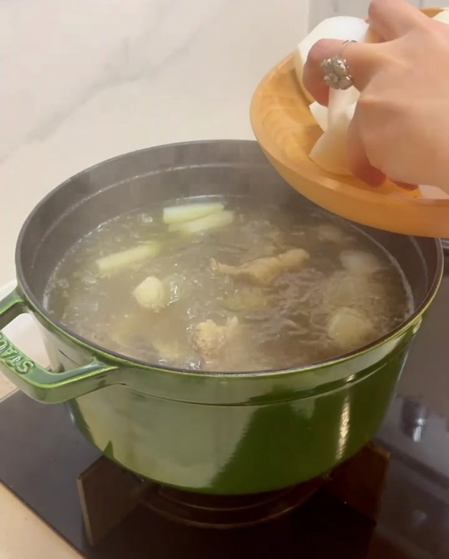 Mano añadiendo trozos blancos grandes de rábano coreano pelado en una olla hirviendo de sopa de res.